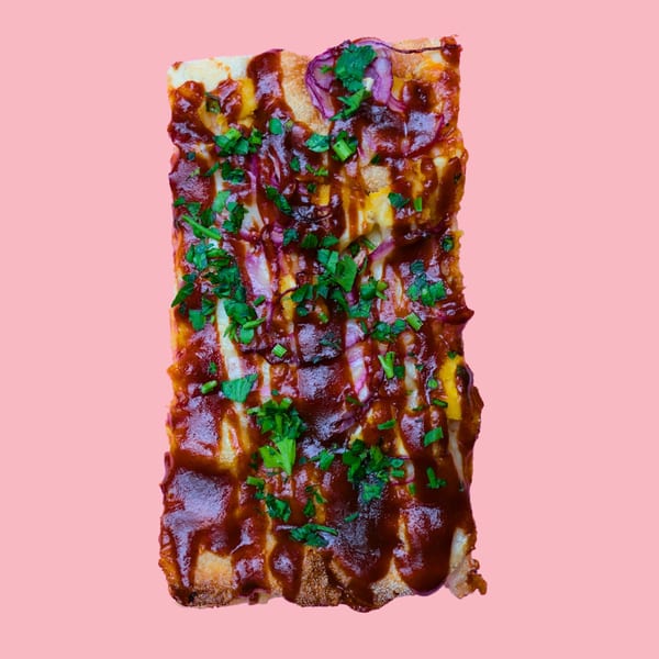 A rectangular slice of BBQ chicken pizza with red onions and cilantro on a pink background.