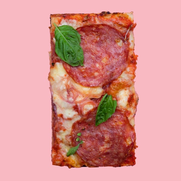 A rectangular slice of pepperoni pizza with melted cheese and fresh basil leaves on a pink background.