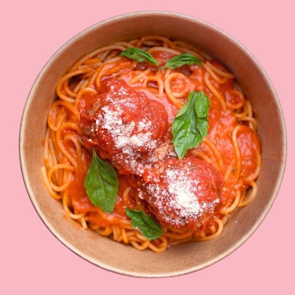 Spaghetti with meatballs, tomato sauce, parmesan, and basil in a brown bowl on a pink background.