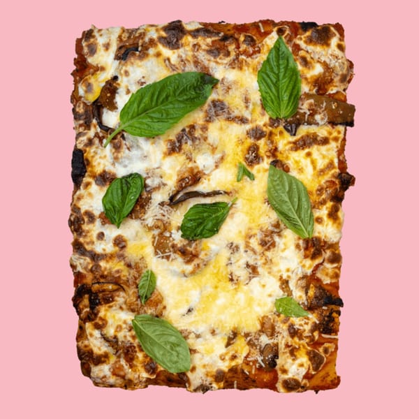 Rectangular baked pasta dish with melted cheese and fresh basil leaves on a pink background.