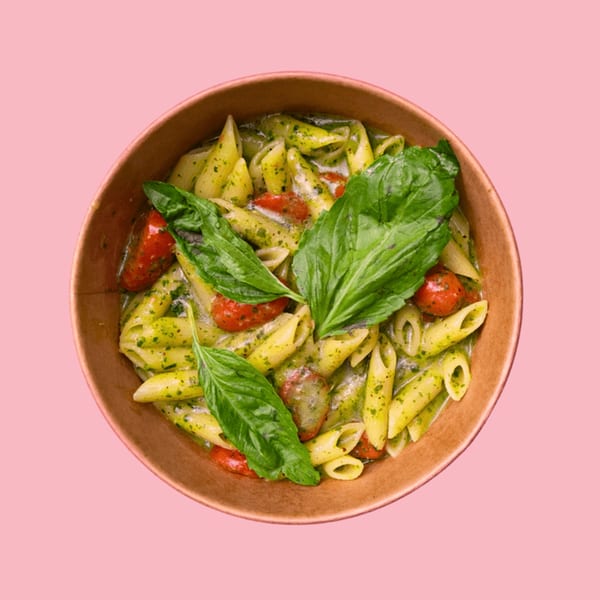 Penne pasta with pesto sauce, cherry tomatoes, and fresh basil in a brown bowl.