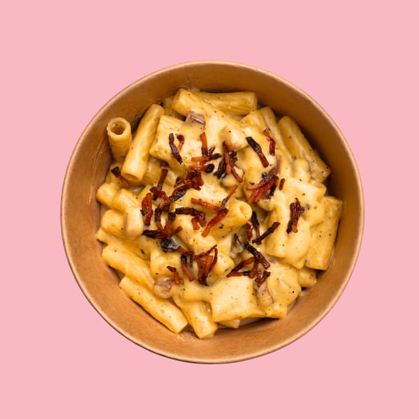 Creamy mac and cheese with crispy bacon bits in a brown bowl on a pink background.