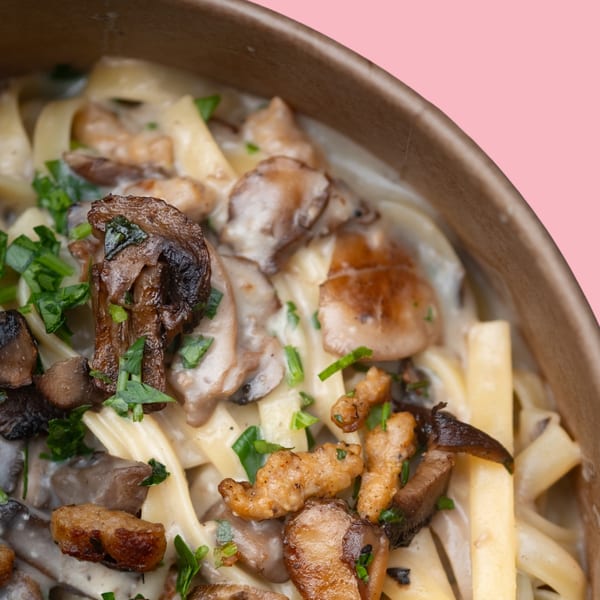 Creamy mushroom pasta with fettuccine noodles and fresh parsley in a brown bowl.