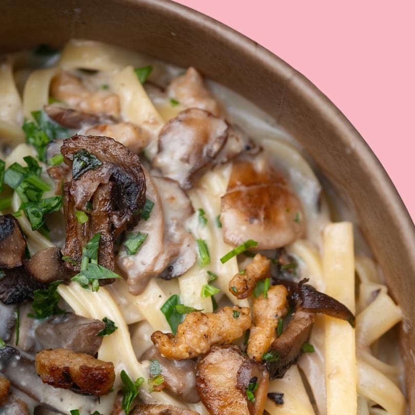 Creamy mushroom pasta with fettuccine noodles and fresh parsley in a brown bowl.
