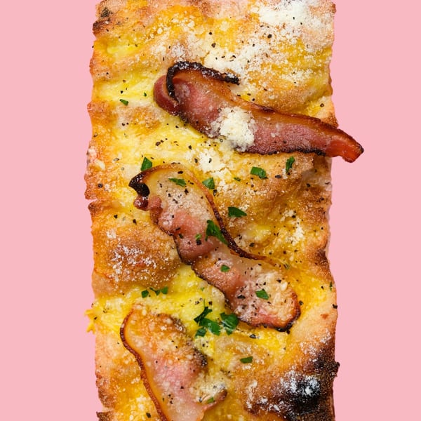 Close-up of a rectangular pizza slice with bacon, cheese, and herbs on a pink background.